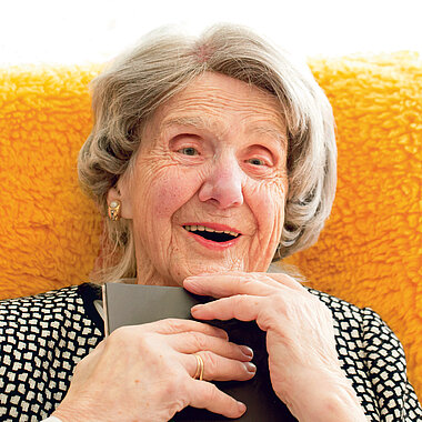 Alte Dame sitzt vor orangem Hintergrund und freut sich